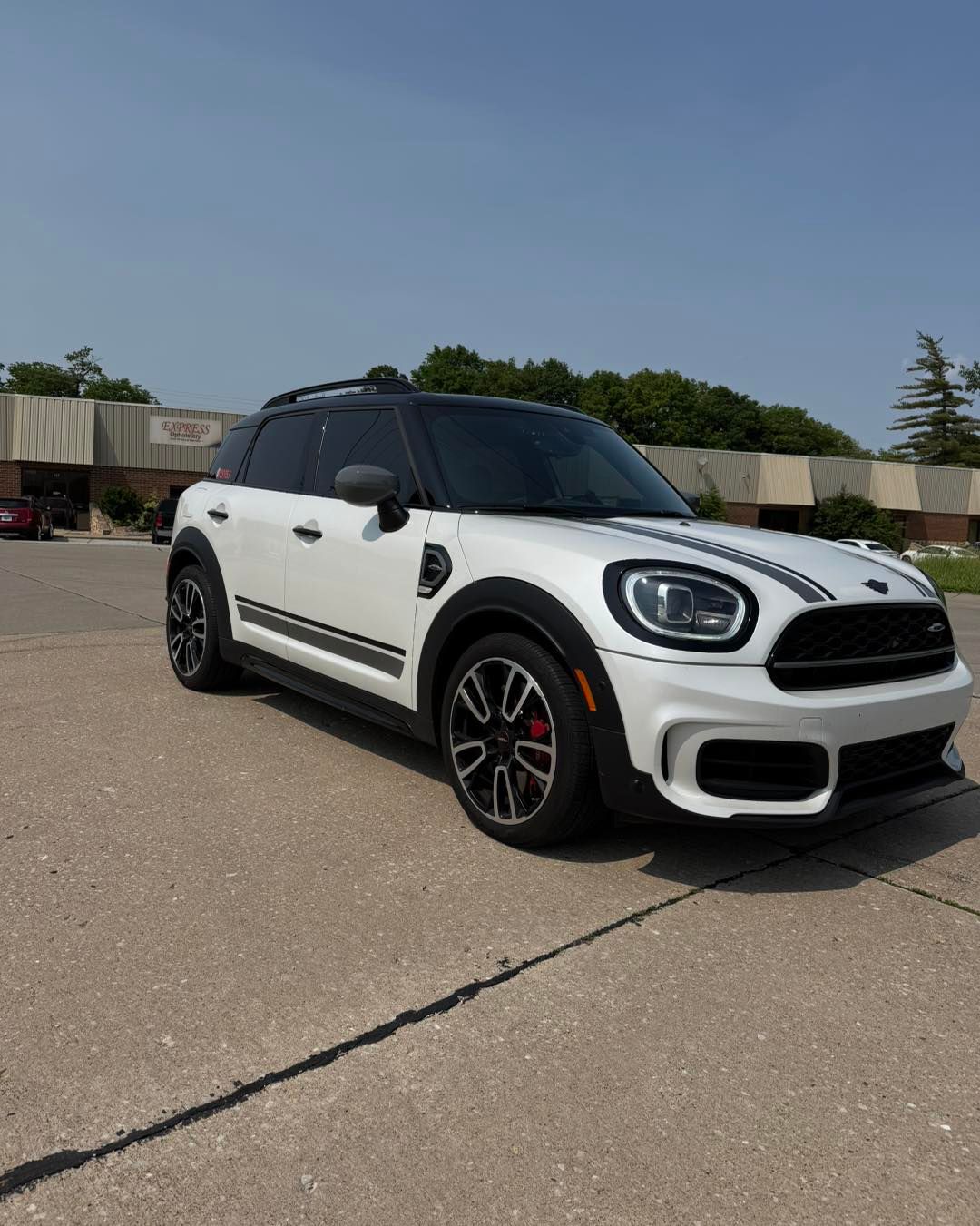 White Mini Cooper parked on pavement under a clear sky, side view with black roof and red accents