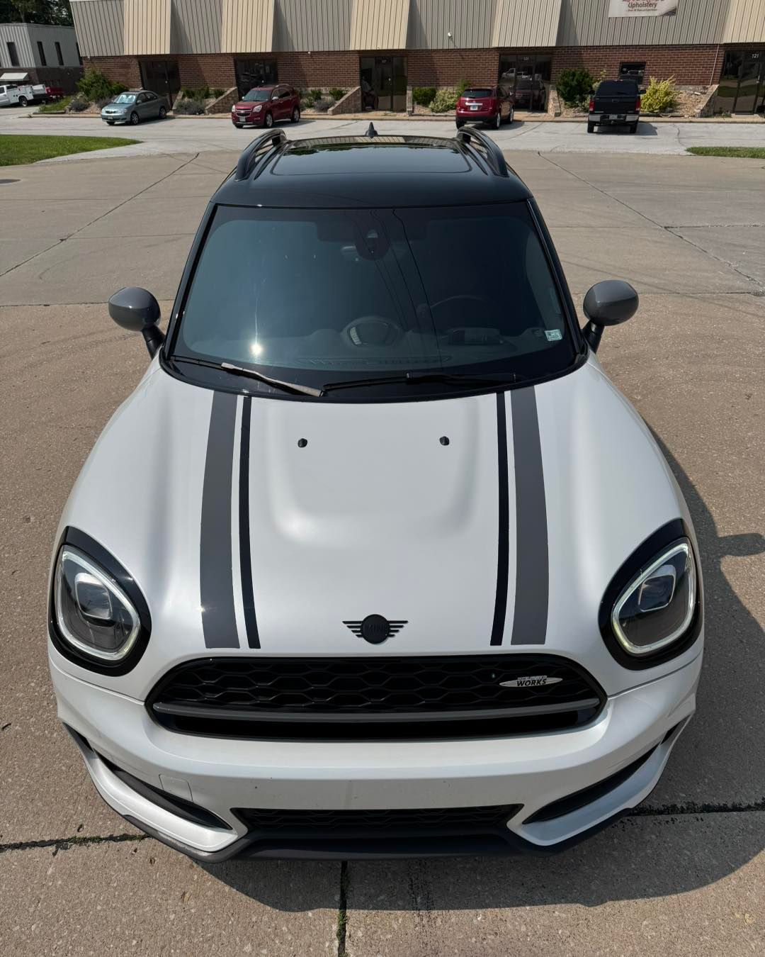 White sports car with black racing stripes parked outdoors on a paved lot