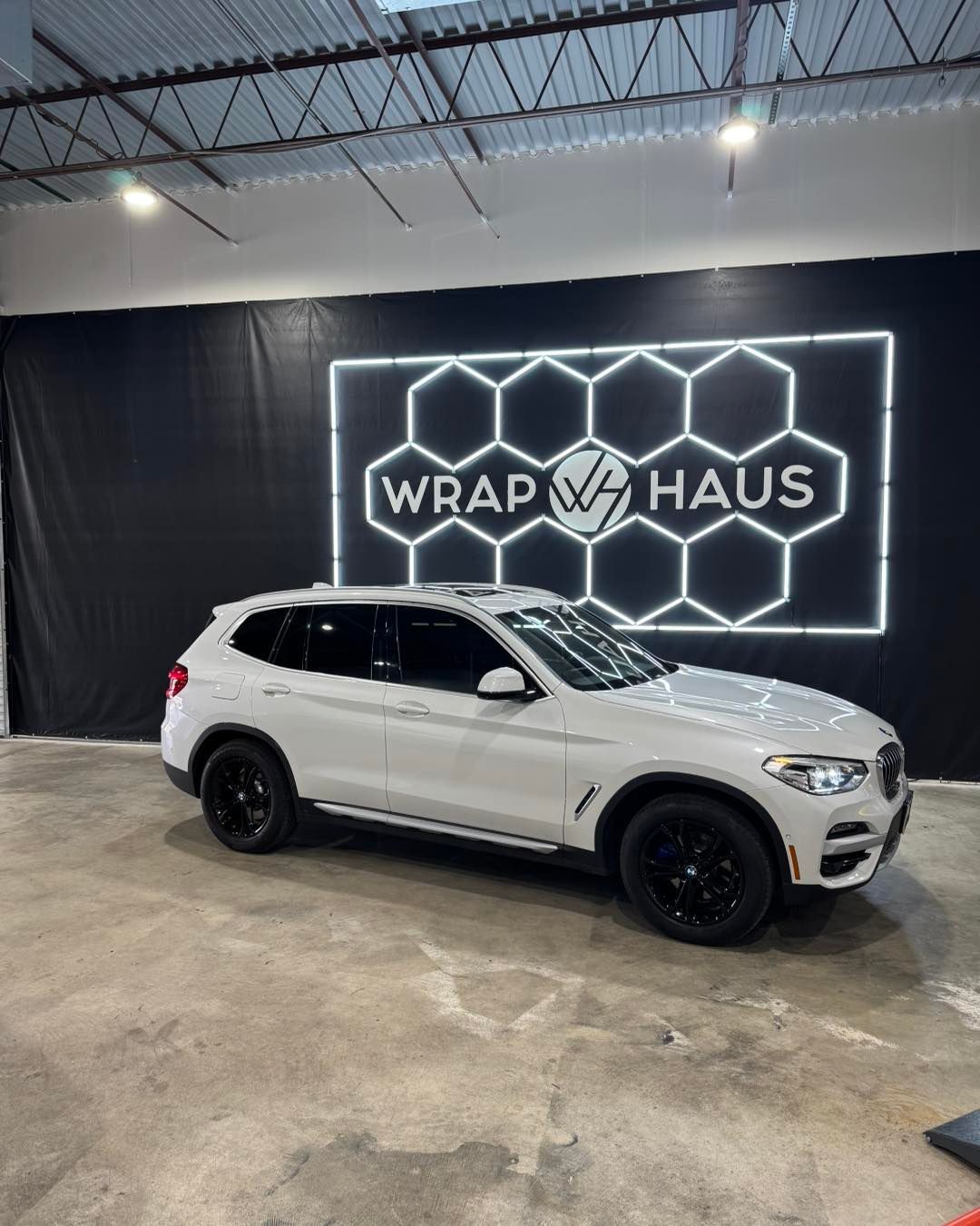 White SUV in a garage showroom with a glowing “WRAP VAHUS” sign on a black wall.
