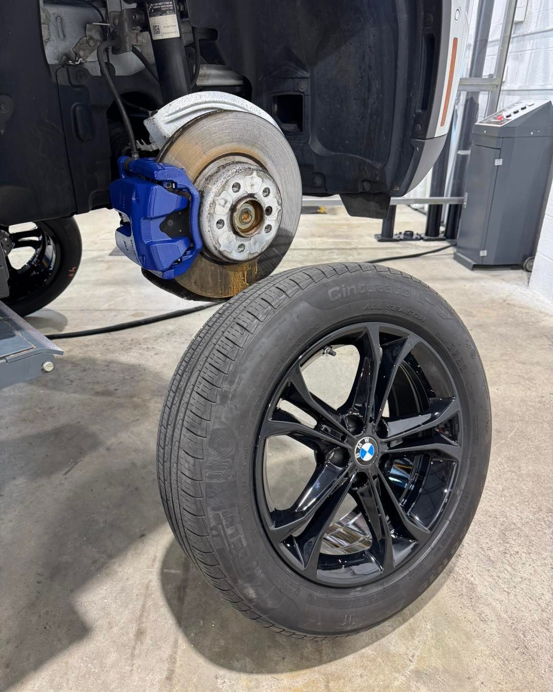 BMW wheel and tire leaning in front of a car with the brake rotor exposed in a repair shop