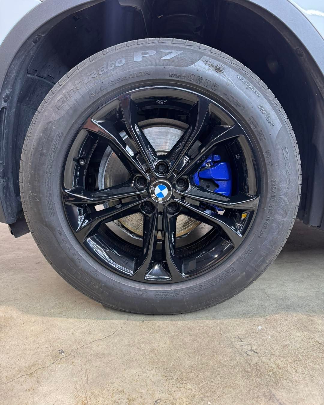 Black BMW wheel with blue brake caliper on a car parked in a garage
