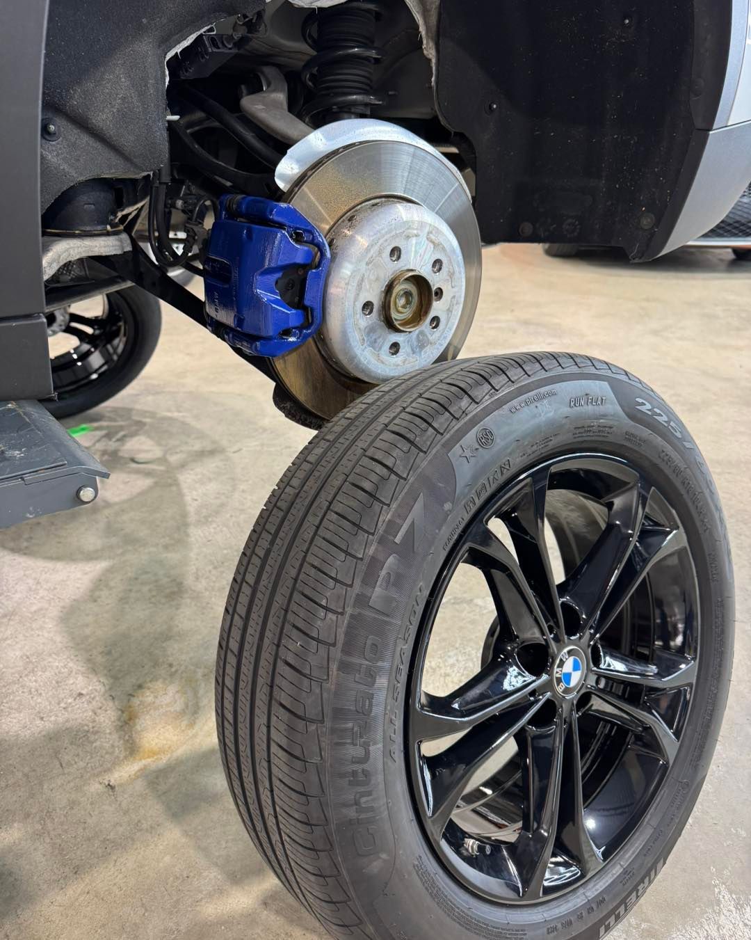 Car wheel removed, showing brake rotor and blue caliper beside a black wheel on a garage floor