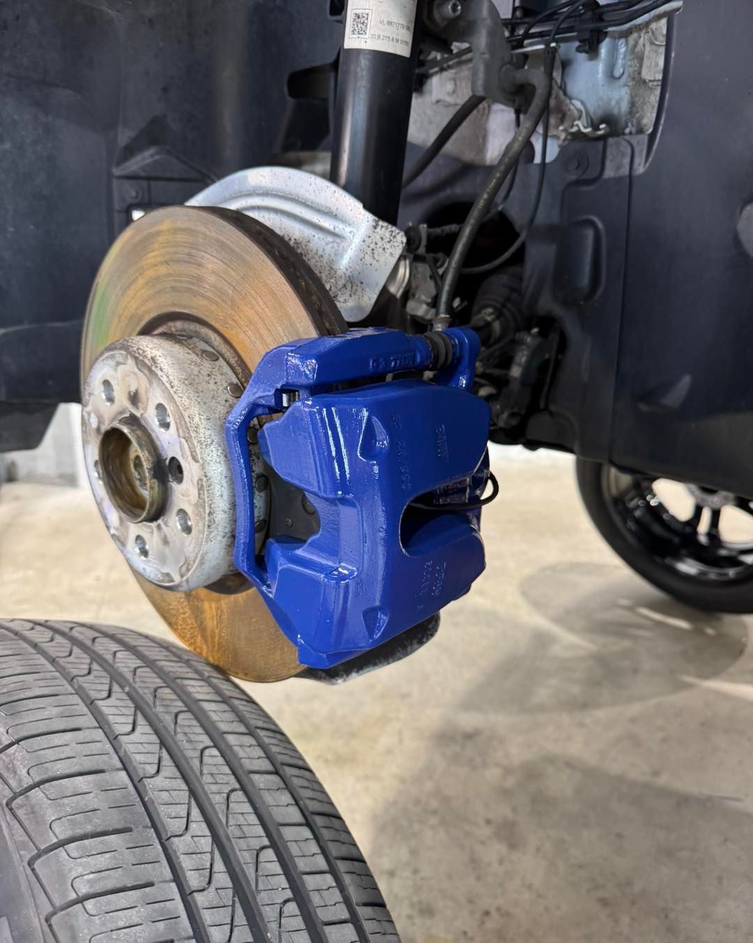 Close-up of a car’s front brake rotor and blue caliper with a wheel removed in a garage.
