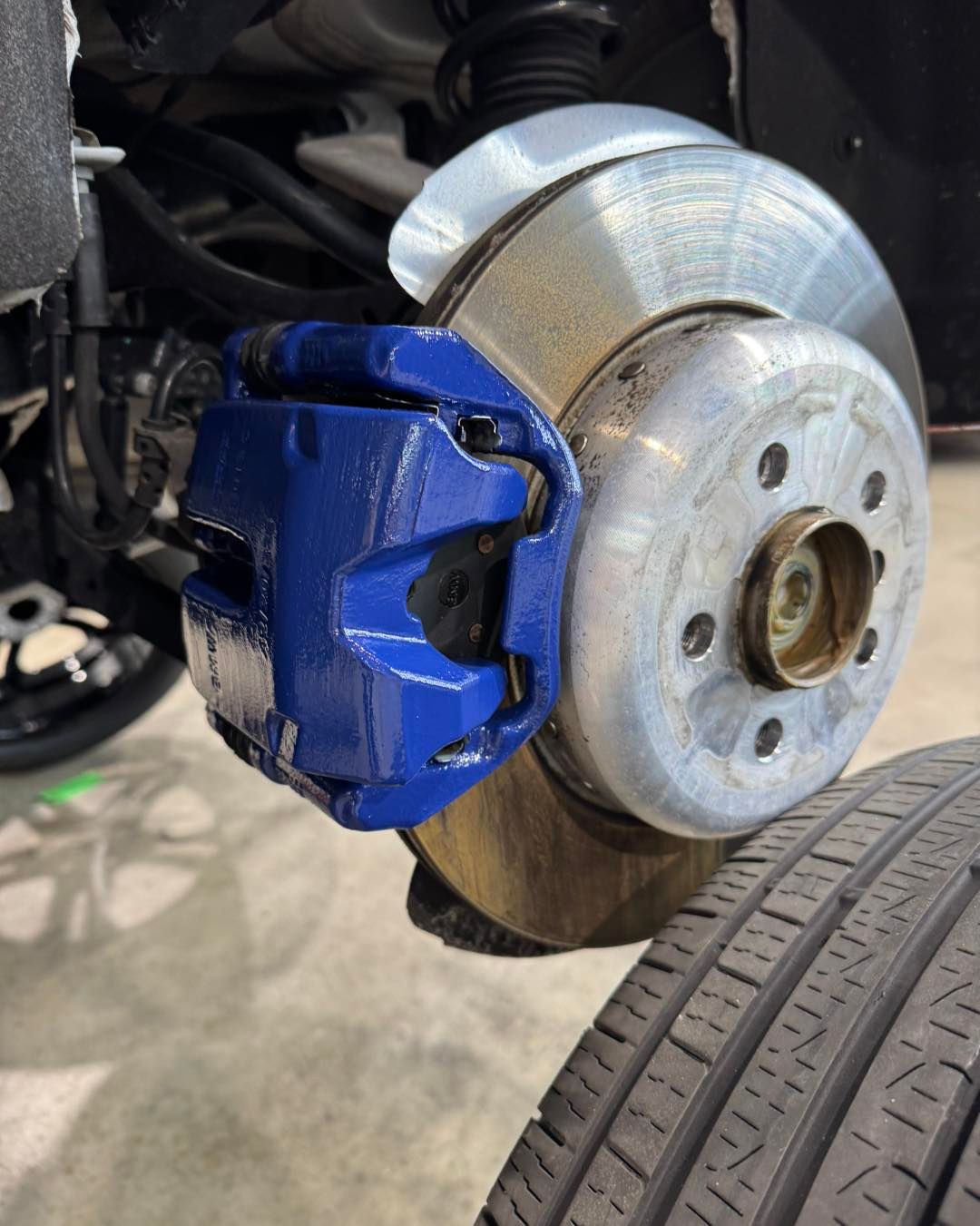 Close-up of a car brake rotor and blue caliper beside the tire and wheel hub
