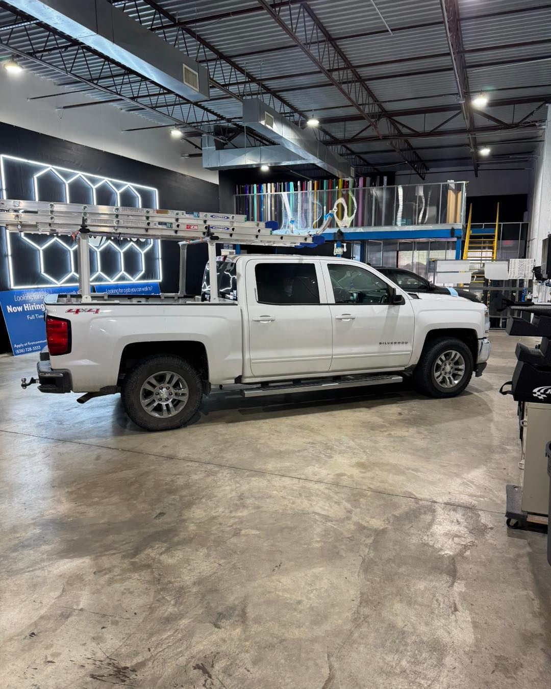 White pickup truck in a garage with shelves and equipment under bright overhead lights