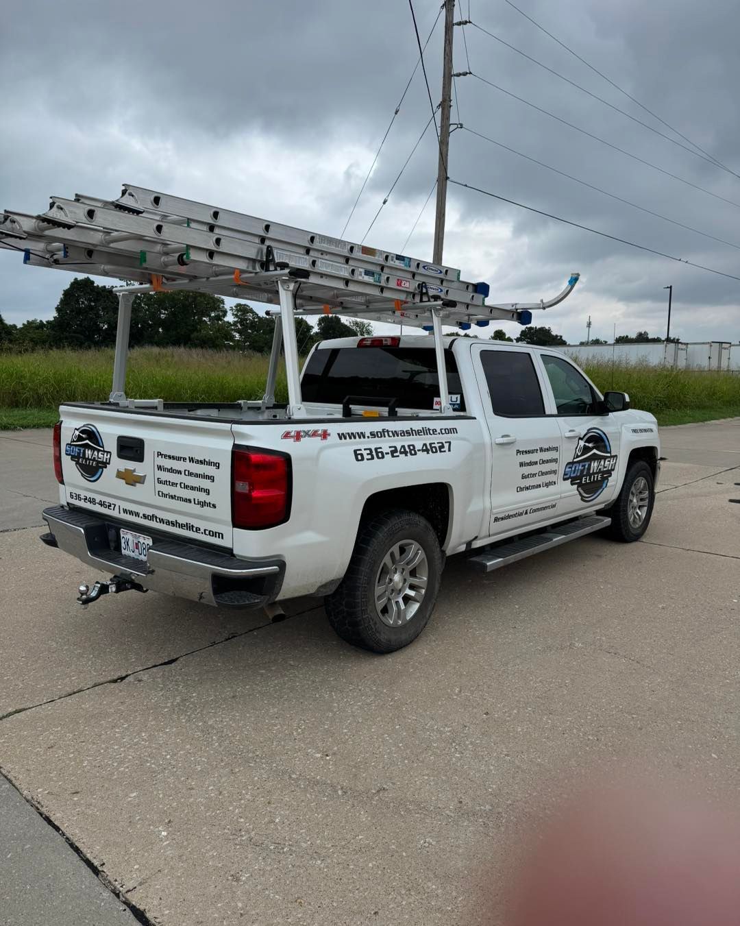 White utility pickup truck with ladder rack parked on a cloudy roadside near power lines