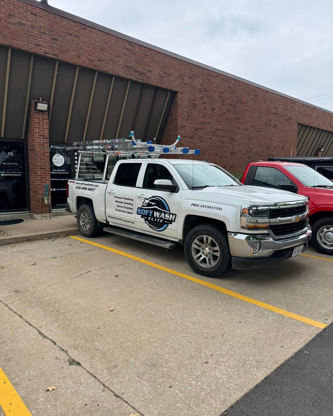 White service truck parked outside a brick building, beside a red SUV in a lot.