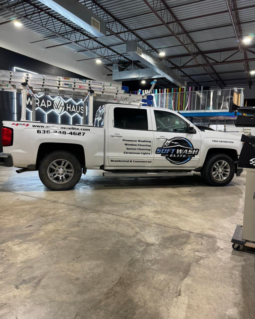 White utility pickup truck with business decals parked inside an industrial garage or warehouse.