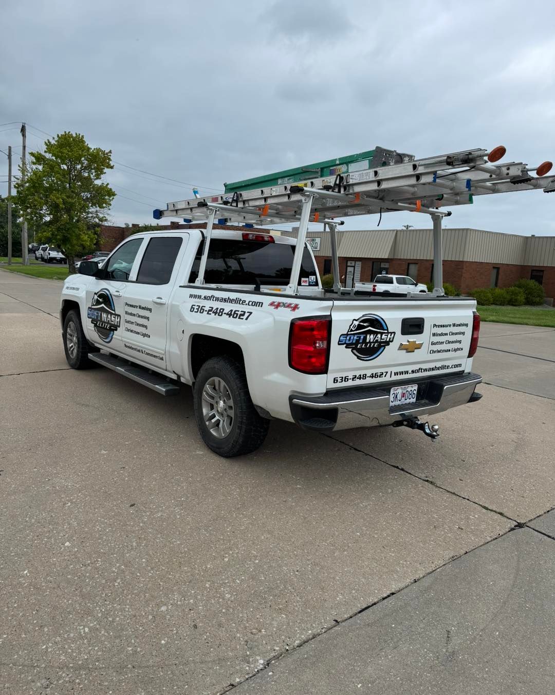 White utility pickup truck with ladder racks parked on a street under cloudy skies.