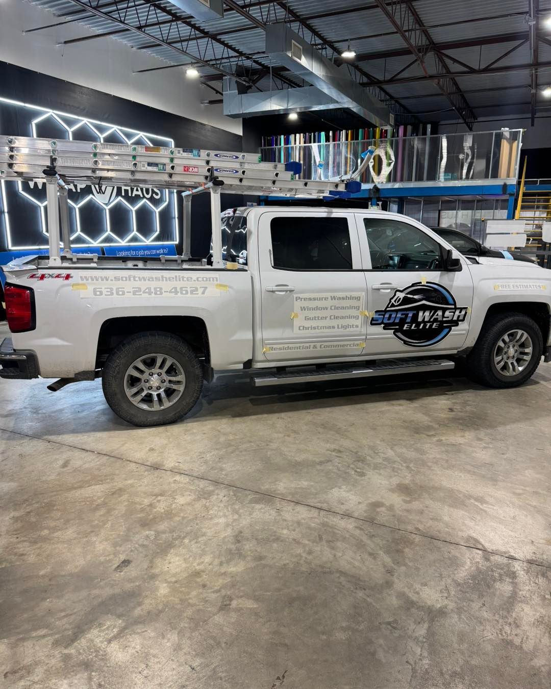White utility pickup truck with company logos parked inside a garage, viewed from the side.