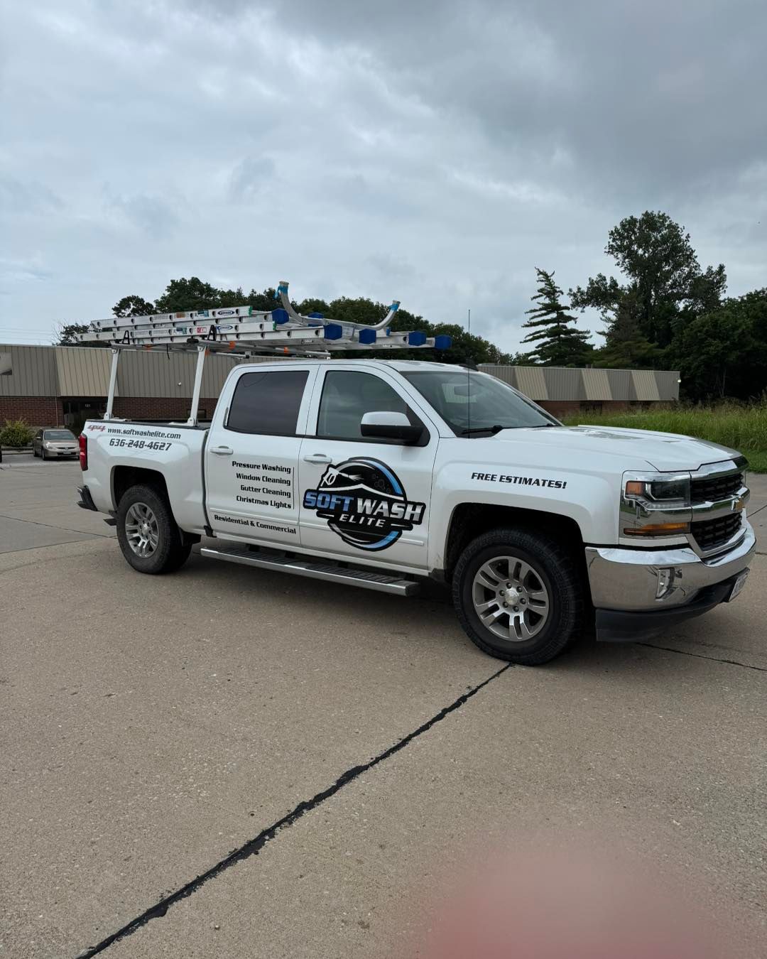White service pickup truck parked on pavement under cloudy sky, with utility racks and company logos.