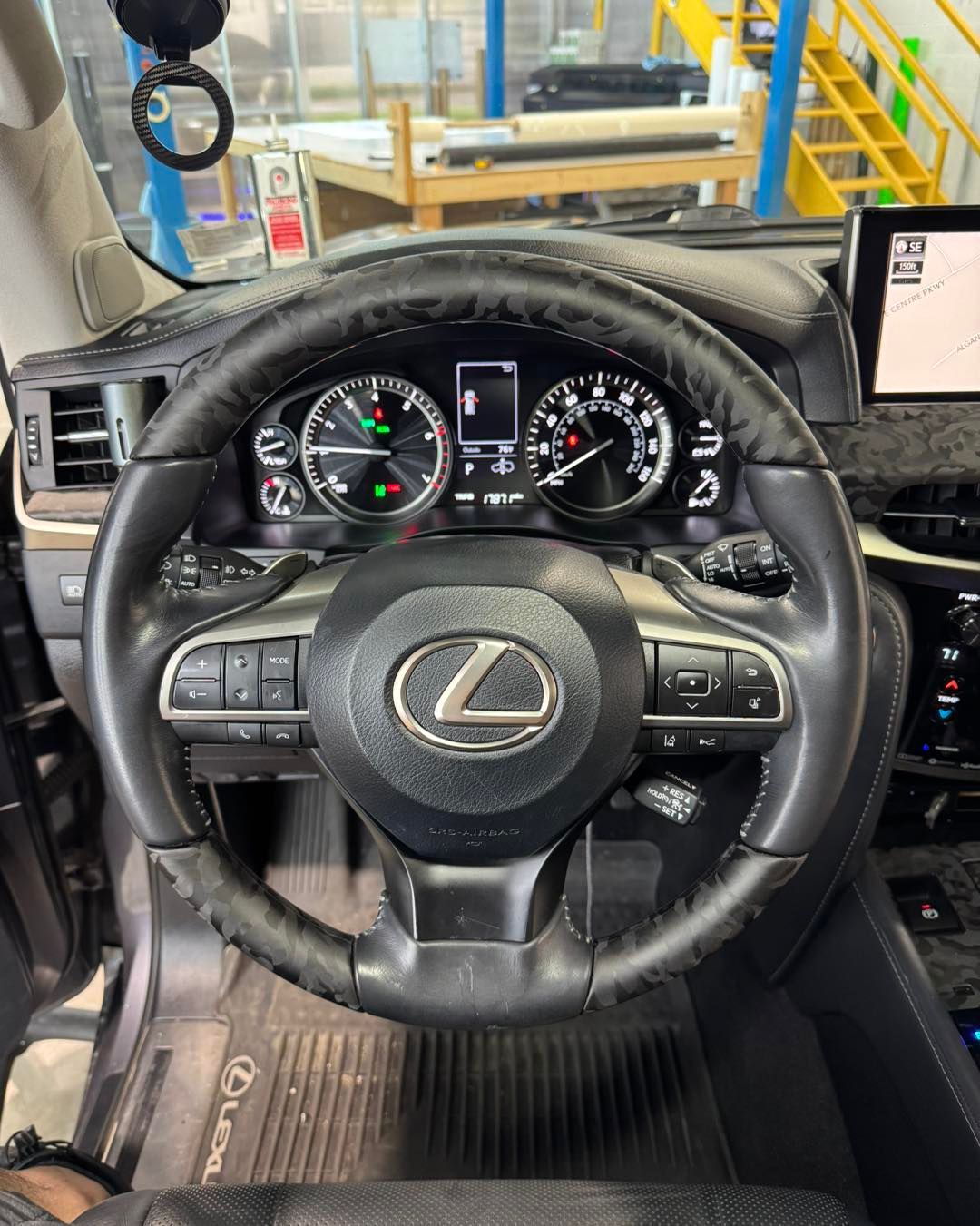 Lexus car interior with steering wheel, dashboard gauges, and center display visible.