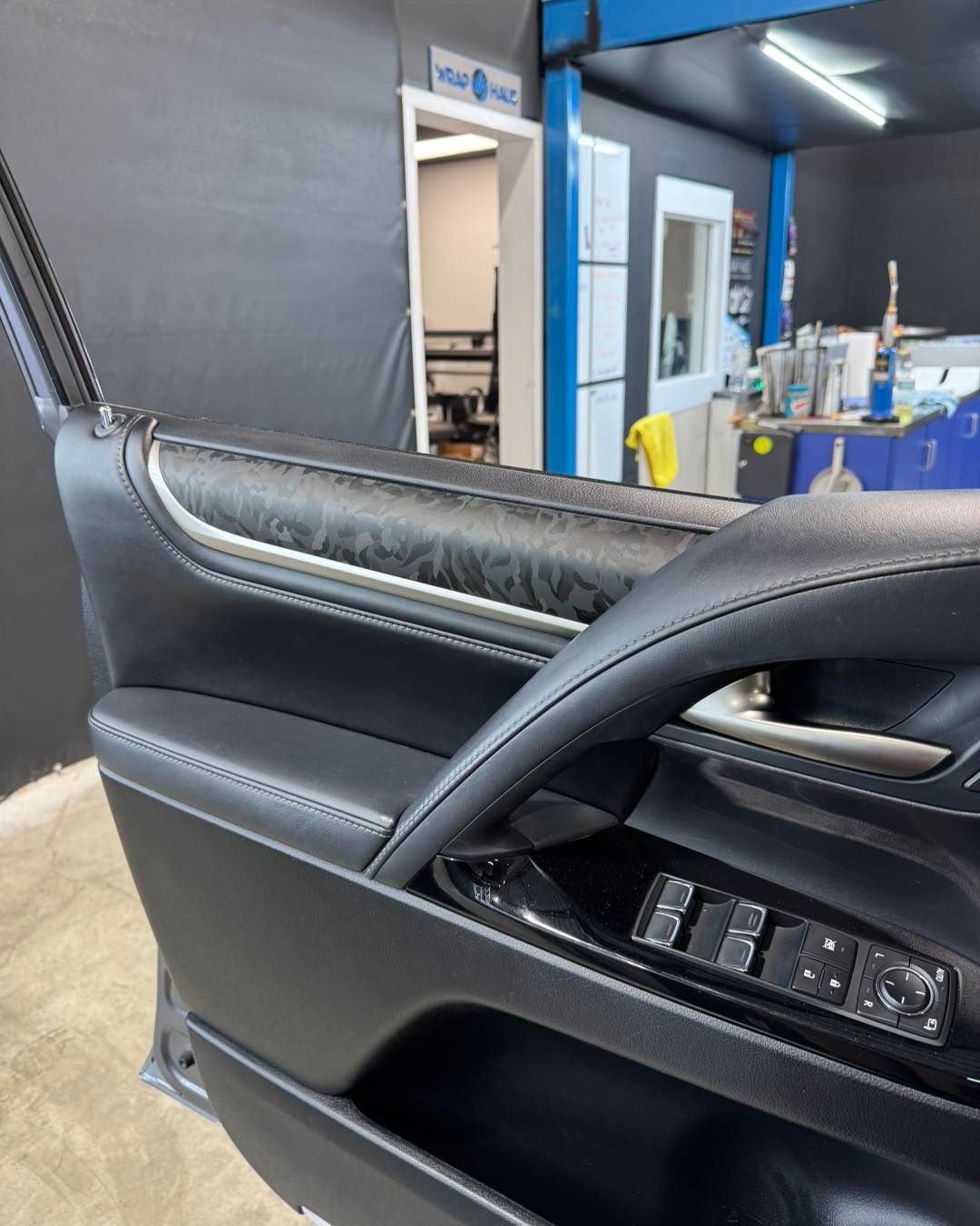 Black leather car seat in a workshop, with a door open and a blue machine in the background