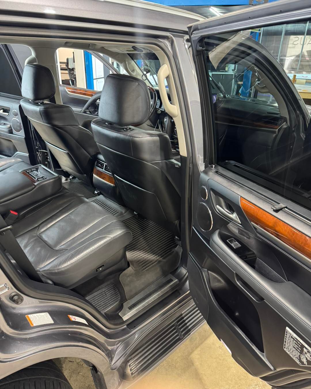 Open car rear door showing black leather seats and wood trim inside a vehicle.