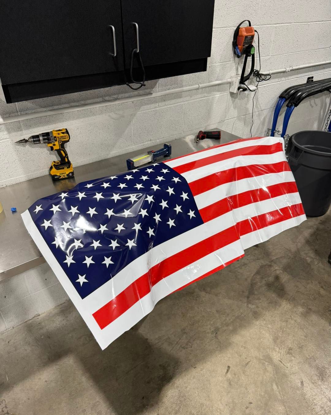 American flag draped over a workbench in a garage with tools and cabinets in the background
