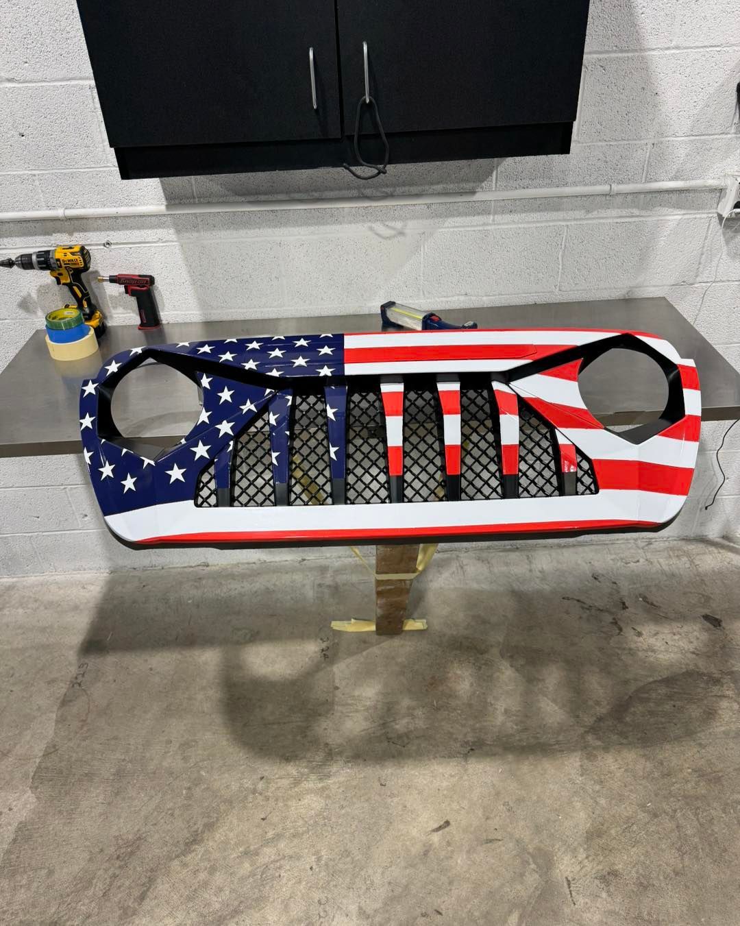 American flag-themed padded cover with two cutout openings, mounted on a wall in a garage-like space