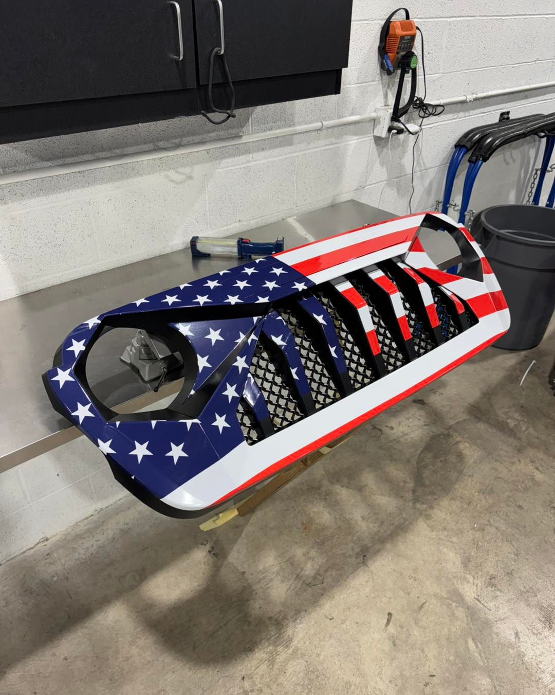 Custom car body panel painted with an American flag design, sitting in a workshop.