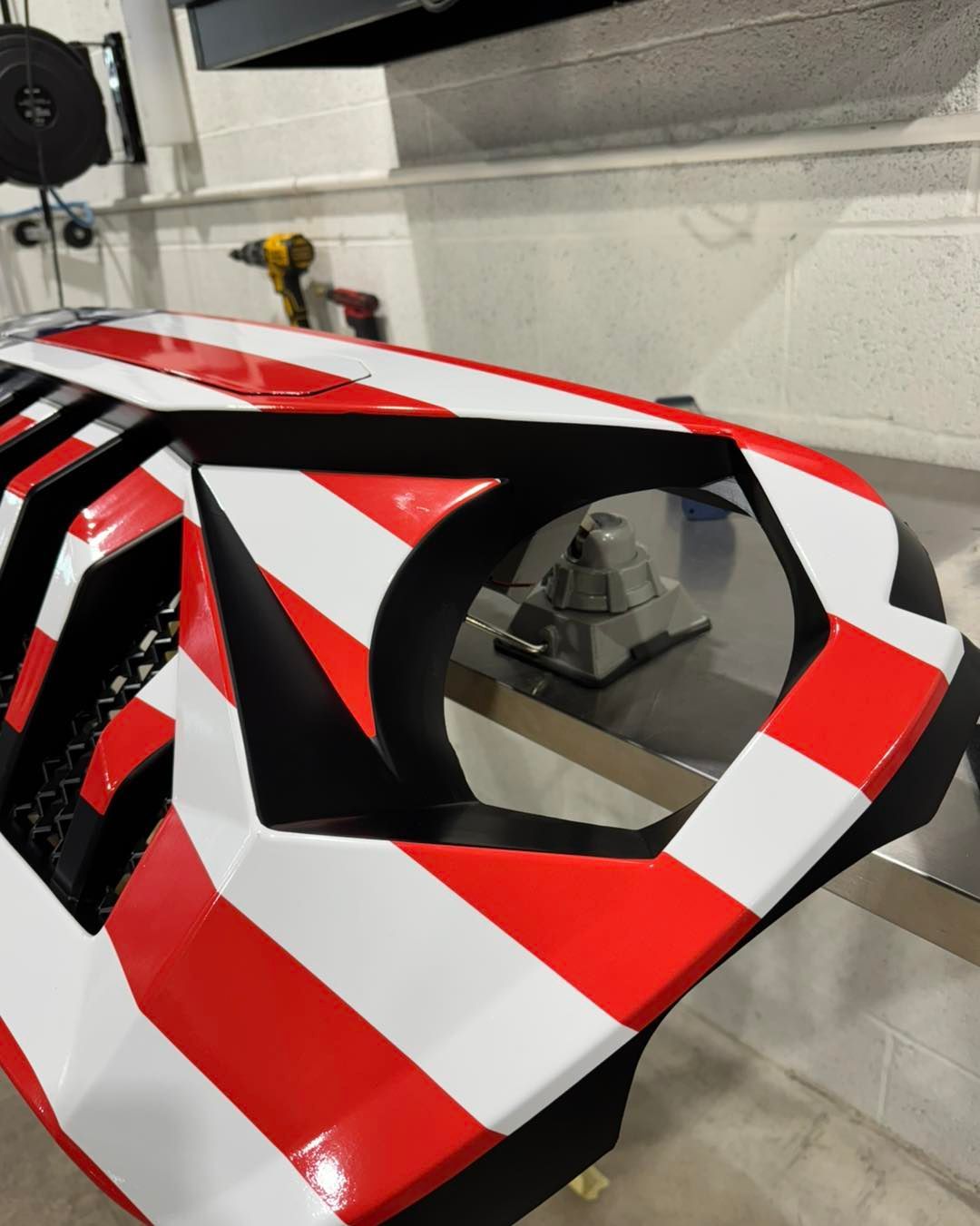 Red, white, and black striped racing shell under construction in a workshop