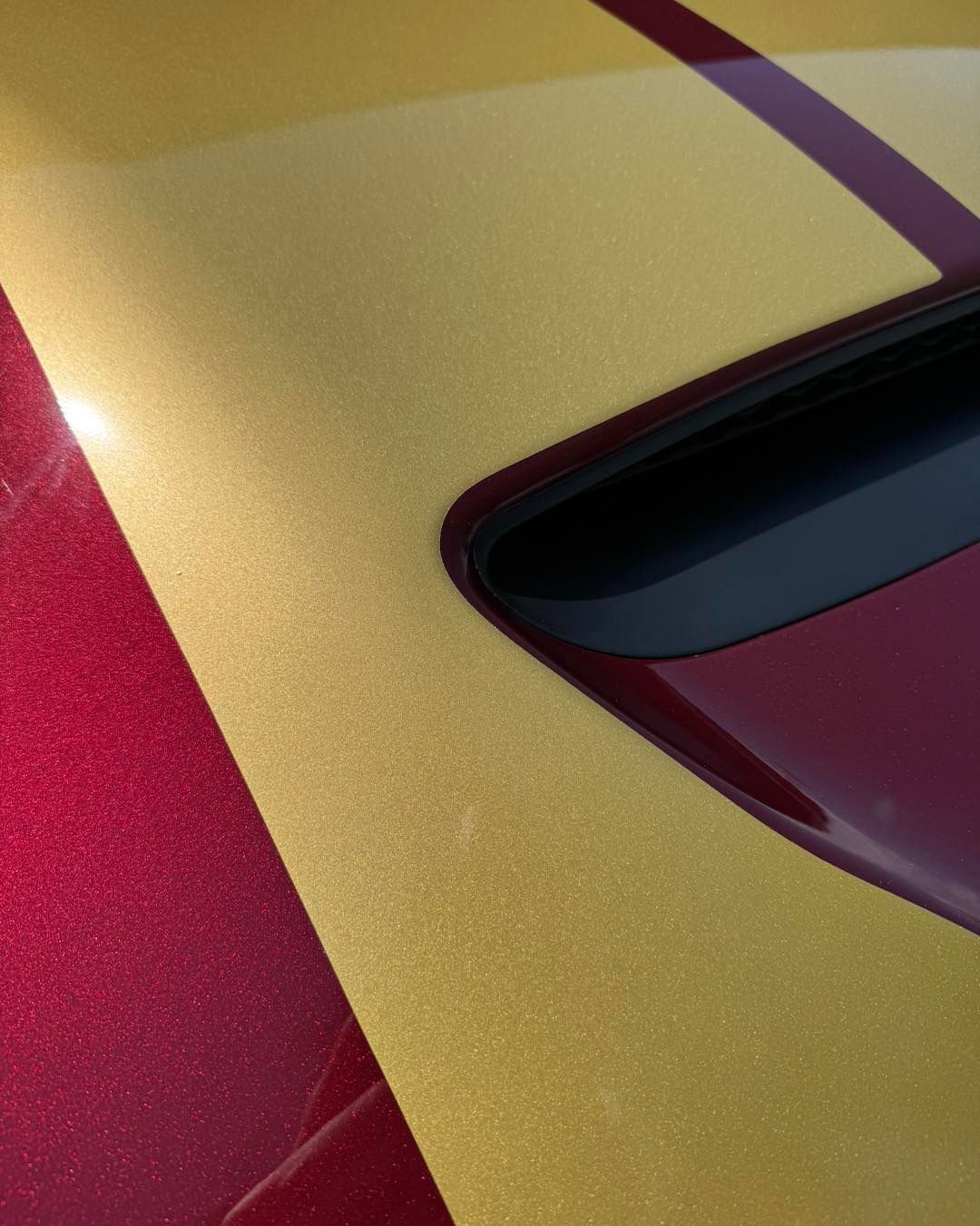 Close-up of a red sports car with a gold racing stripe and black window trim