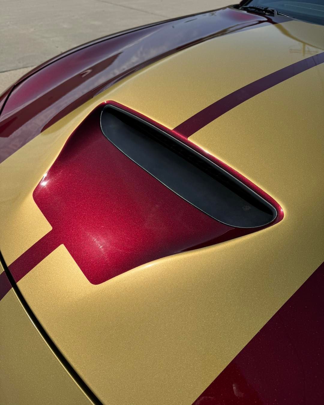 Close-up of a gold and burgundy car hood with a black air vent