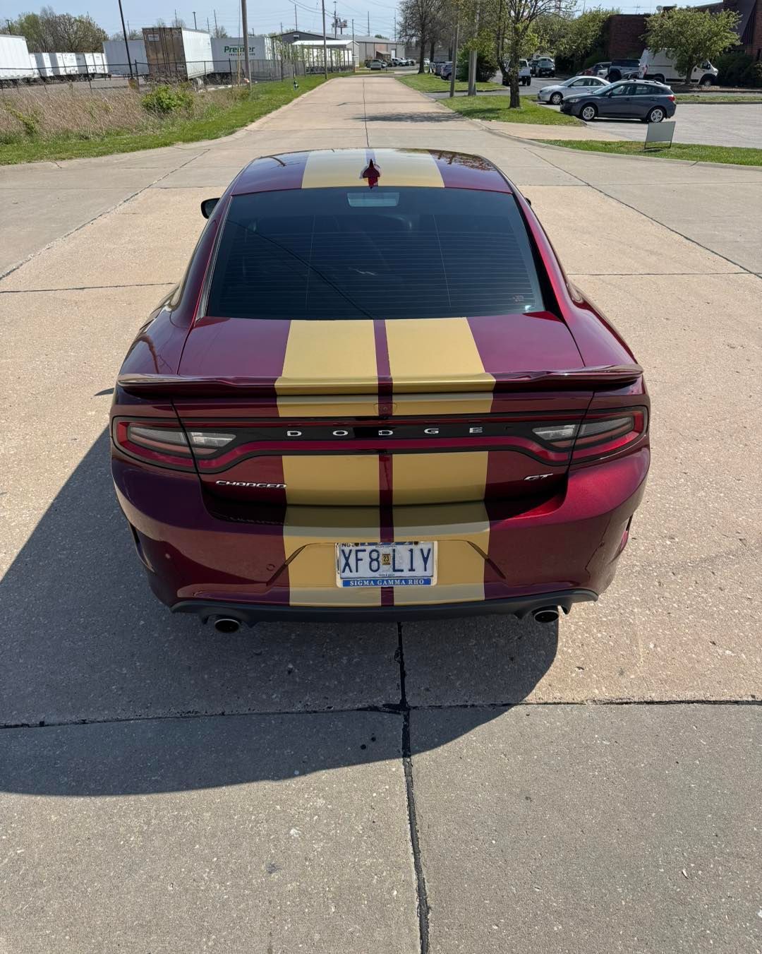 Rear view of a maroon sports car with gold racing stripes parked on a road.