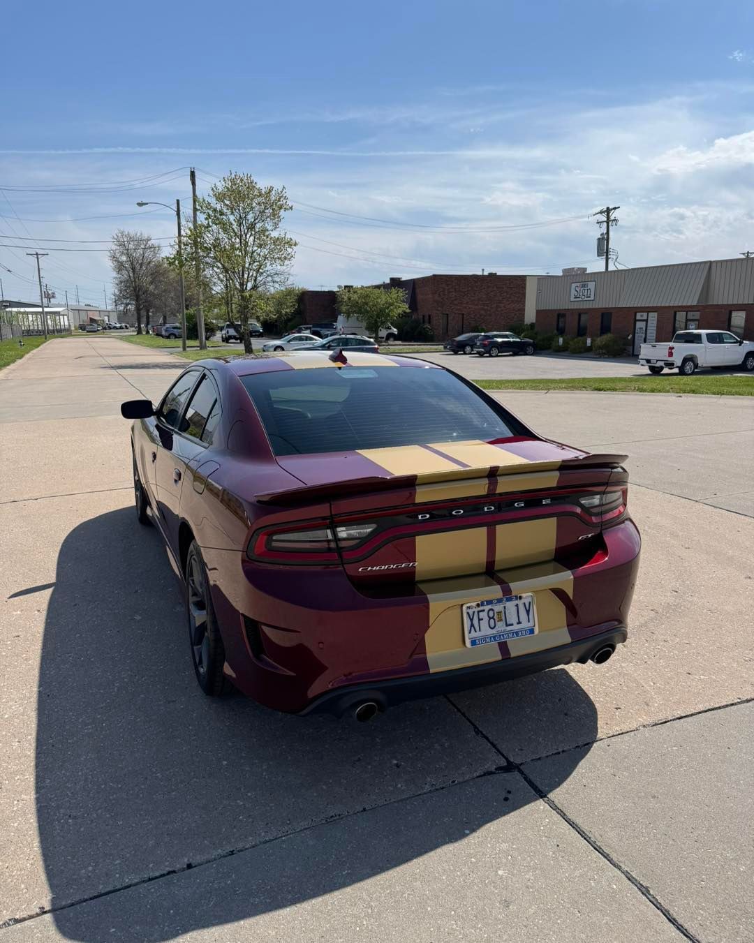 Maroon sports sedan with gold racing stripes parked on a sunny street