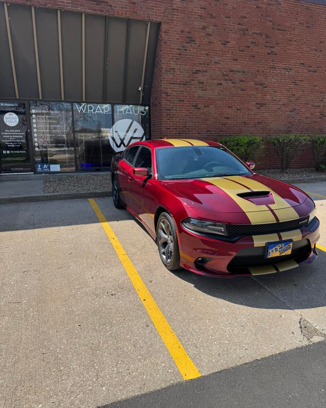 Red sports car with black racing stripe parked in front of a brick storefront.