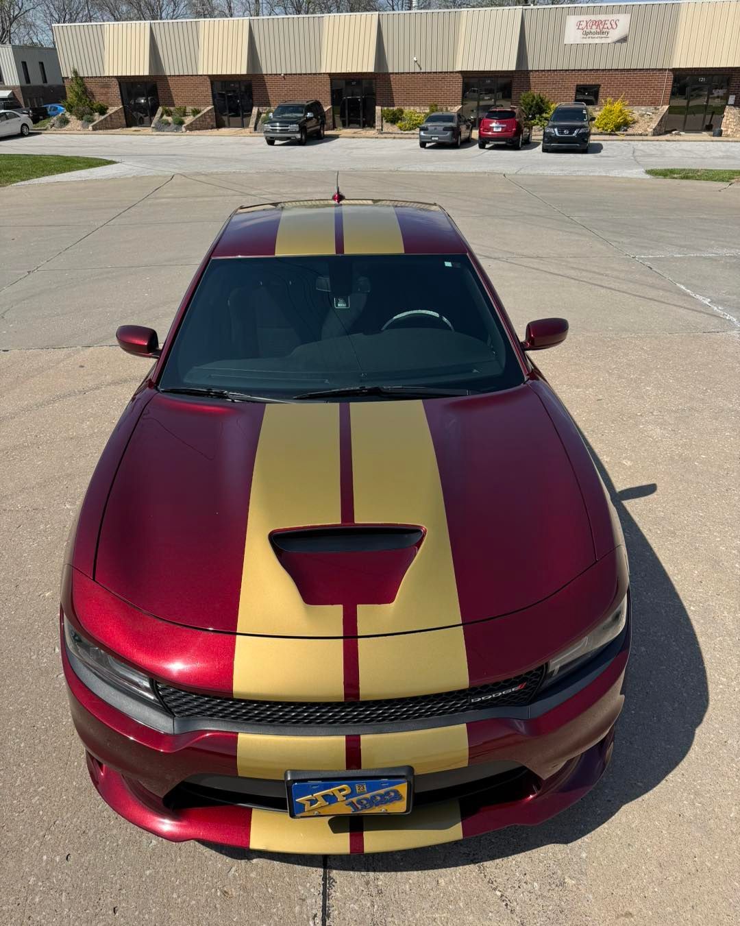 Maroon car with gold racing stripes parked in a lot in front of storefronts.