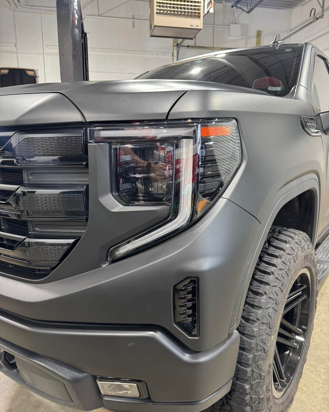 Front view of a matte gray SUV with black grille and off-road tires in a garage