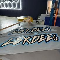 Graffiti-style logo on a light gray surface in a workshop, with black, white, and blue lettering.