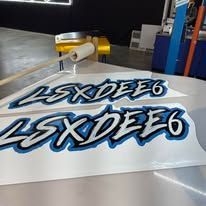 White stickers with blue-and-black “LSXDFE6” text on a print table in a workshop