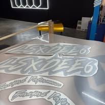 Vinyl decals on a silver surface in a workshop, with a yellow cutting tool and blue machine in the background