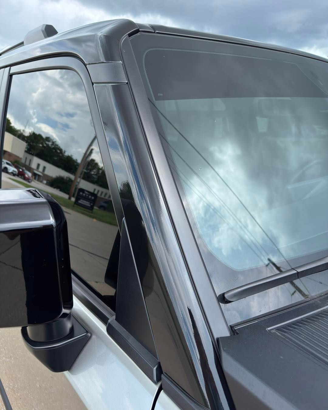 Black SUV windshield and side mirror under cloudy sky