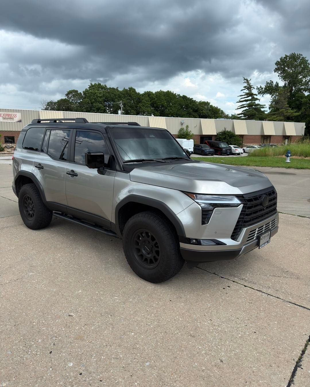 Silver SUV parked on a road under cloudy skies, with trees and a concrete barrier in the background