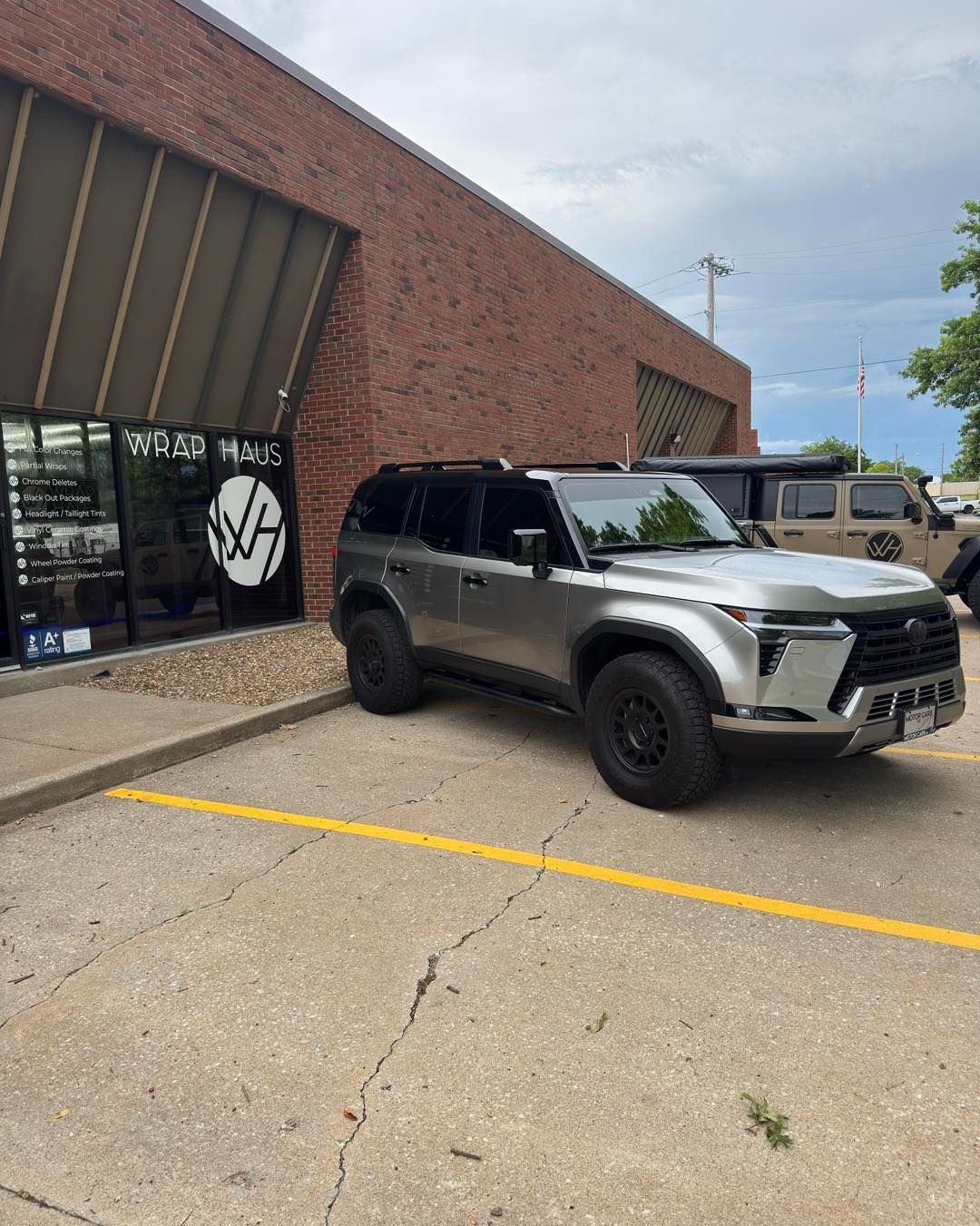 Gray SUV parked outside a brick storefront with a black sign and yellow parking lines.