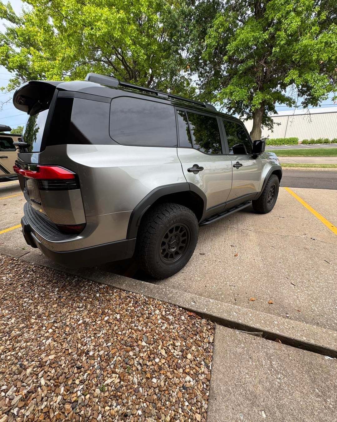 Silver SUV parked beside a curb under trees on a paved lot.