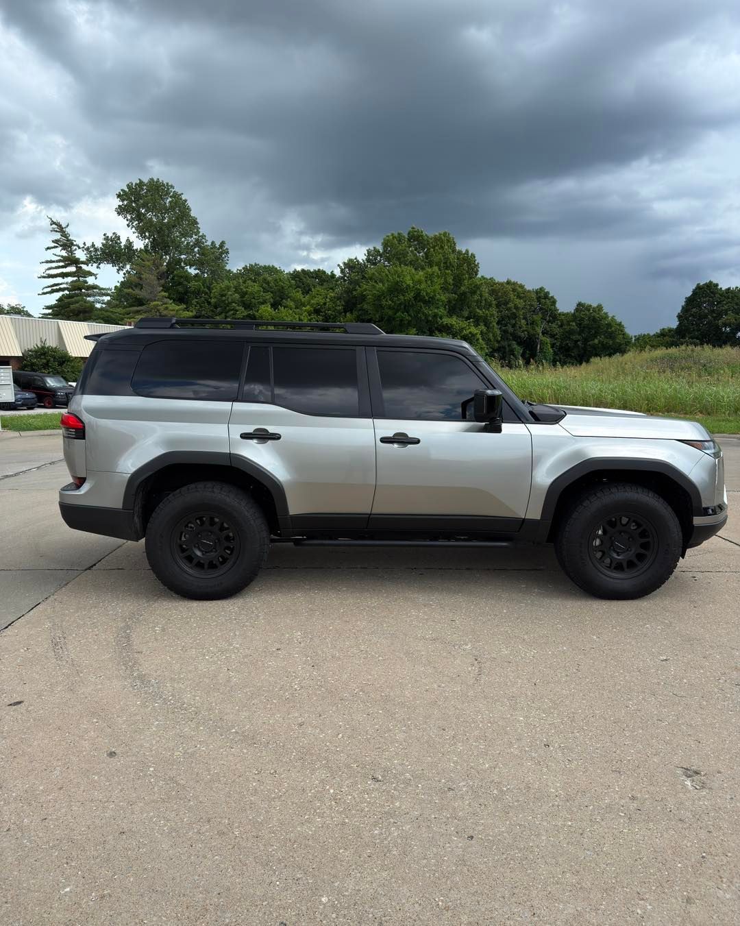 Silver off-road SUV parked on pavement under a cloudy sky, side view