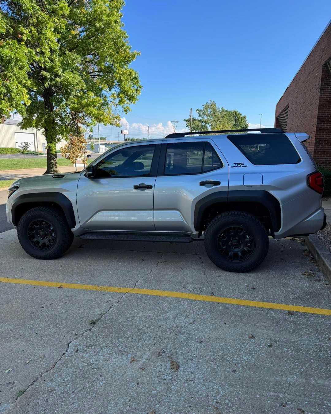 Silver SUV parked in a lot beside a brick building, with a tree and blue sky in the background