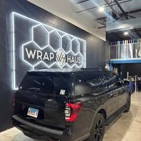 Black SUV parked inside Wrap Haus shop with illuminated wall sign and hexagon logo