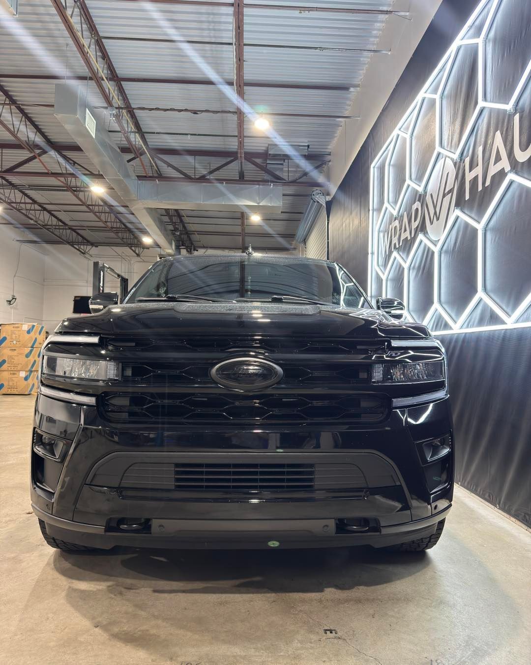 Black SUV parked indoors under bright lights, facing forward in an industrial garage.