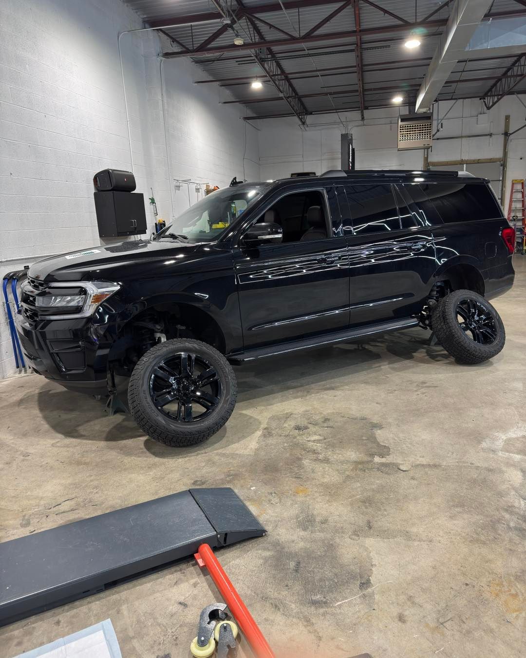 Black SUV on a lift in an auto shop, with a concrete floor and garage equipment around it