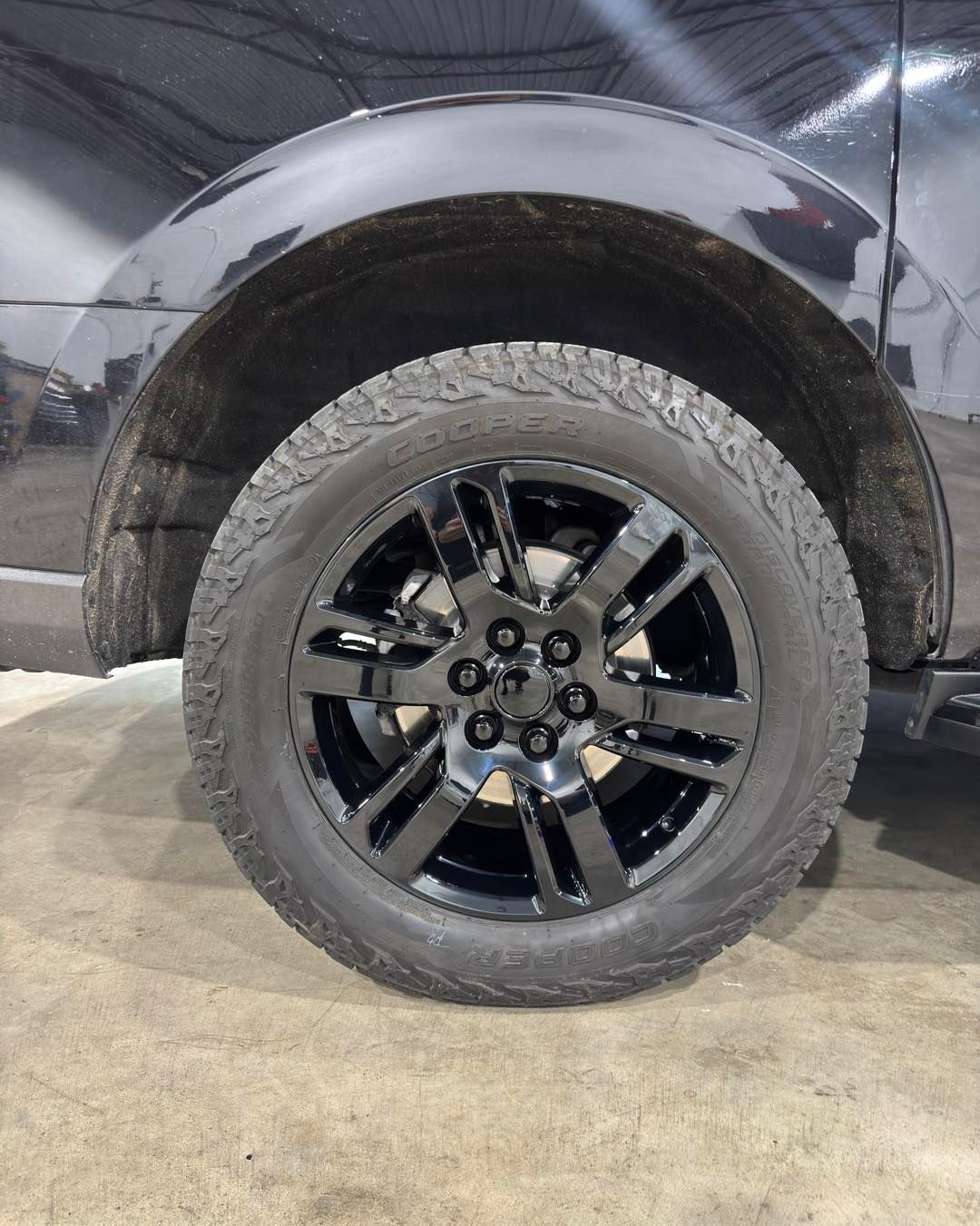 Black truck rear wheel and tire under fender in a garage or shop