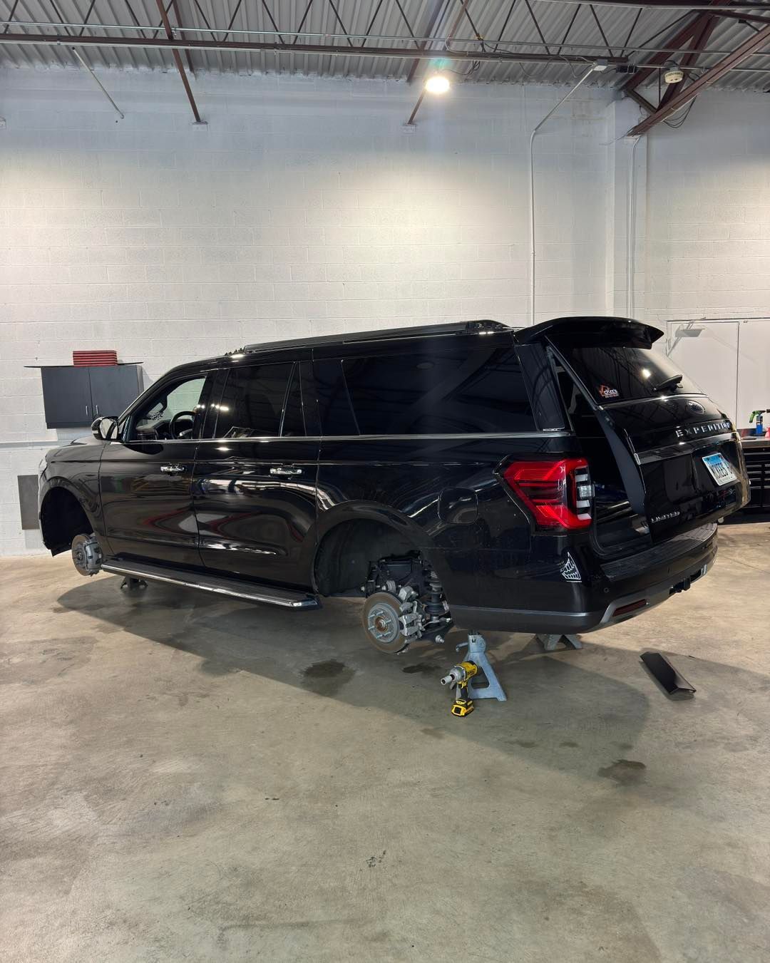 Black SUV in an auto shop on jacks, with a wheel removed and rear hatch open.