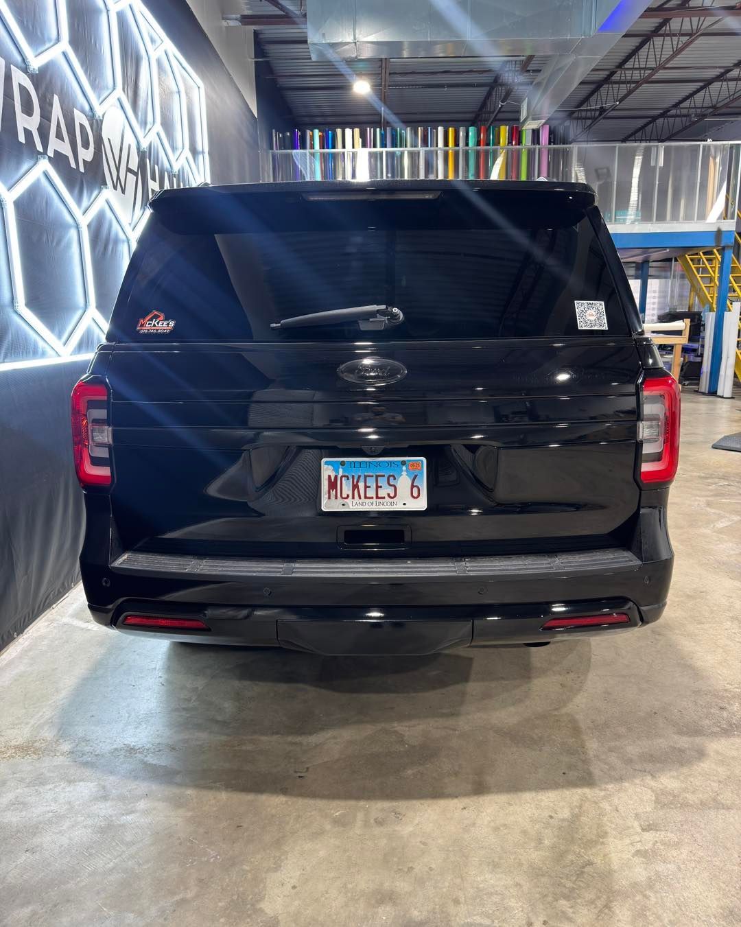 Black SUV viewed from the rear in an indoor parking or showroom space, with illuminated wall decor.