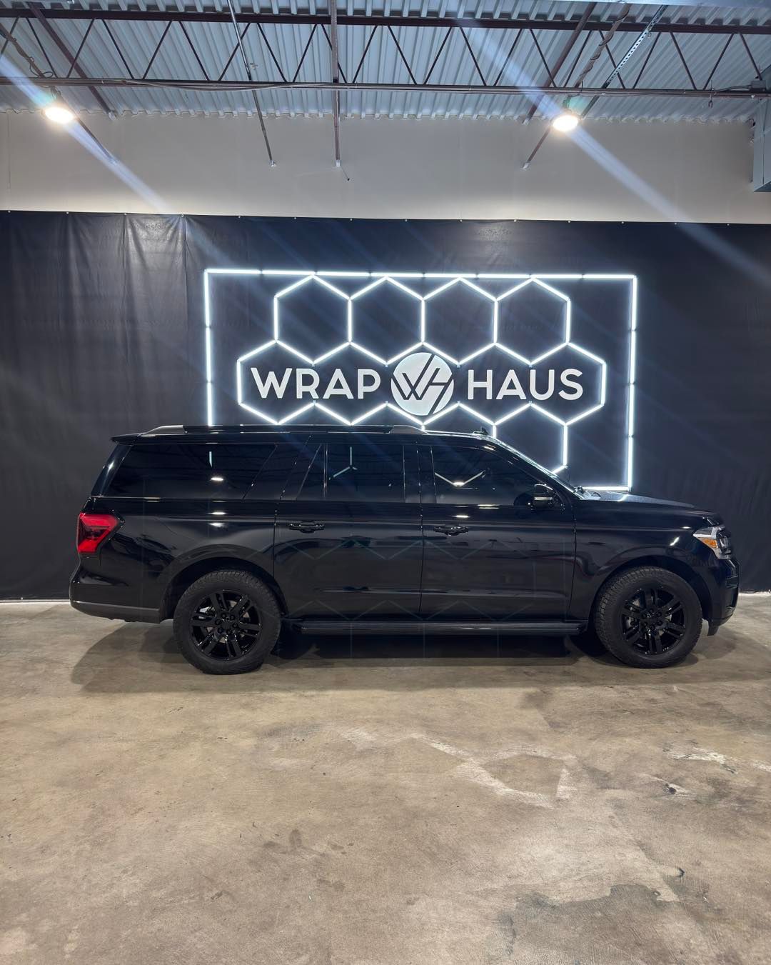 Black SUV in a garage beneath a glowing “Wrap Haus” sign.