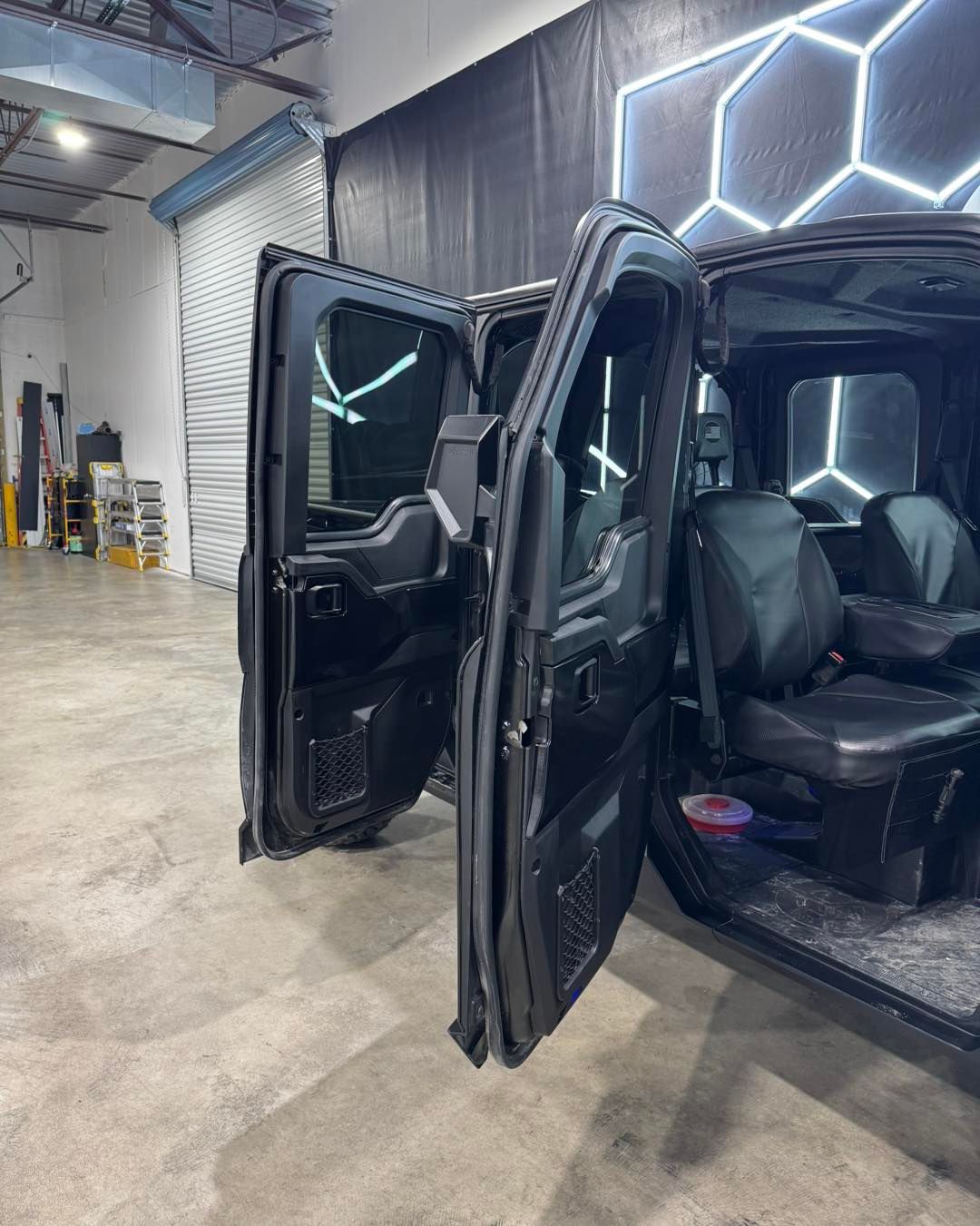 Black SUV with open doors parked indoors near illuminated wall panels.