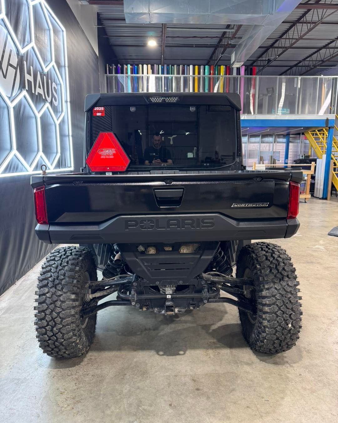 Black lifted pickup truck with oversized off-road tires parked in a warehouse-like garage