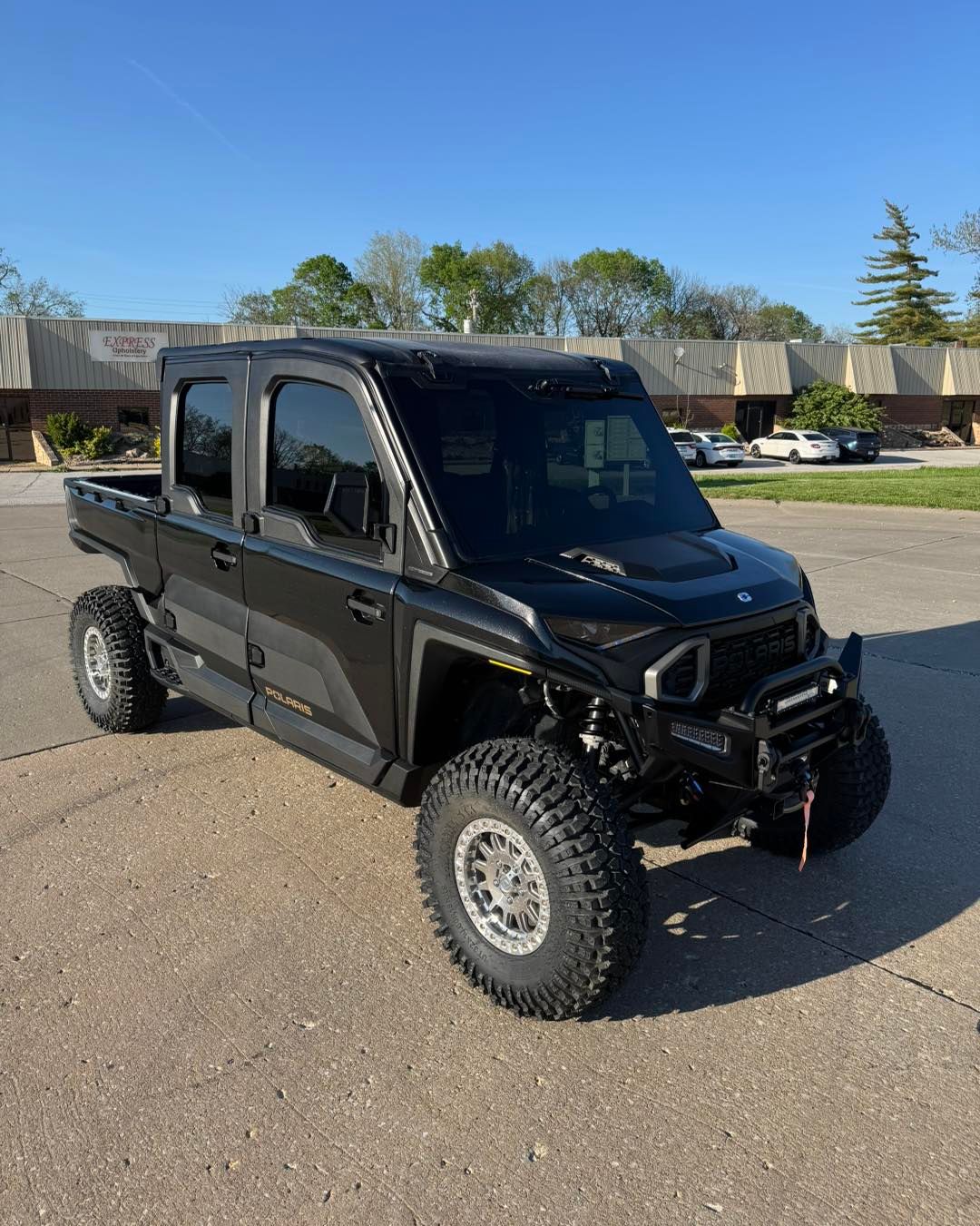 Black lifted off-road utility truck parked on a paved lot under a clear blue sky