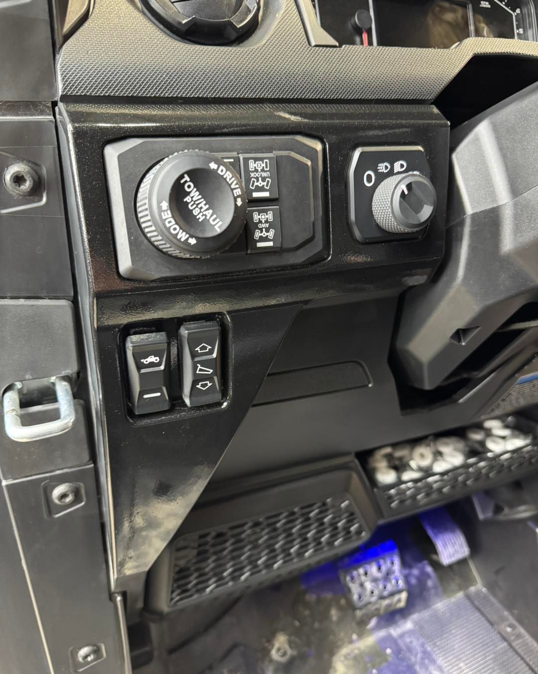 Vehicle dashboard panel with rotary controls and switches on a dark carbon-fiber trim