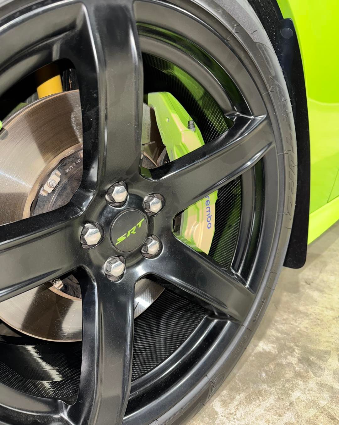 Close-up of a black car wheel rim and brake rotor beside a bright lime-green body panel.